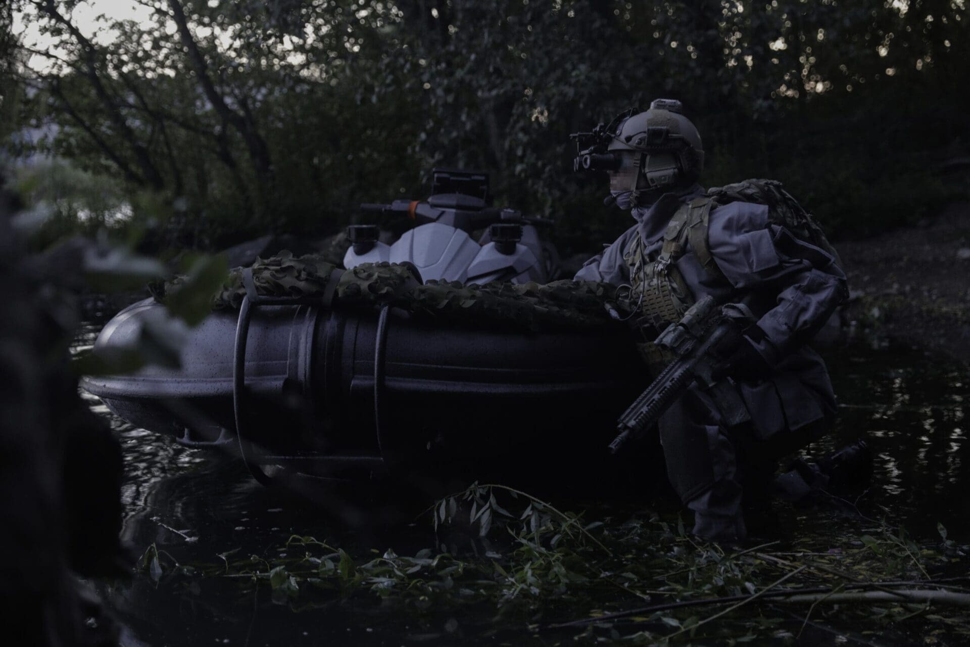 Operator with night vision goggles beside an inflatable boat during a night exercise